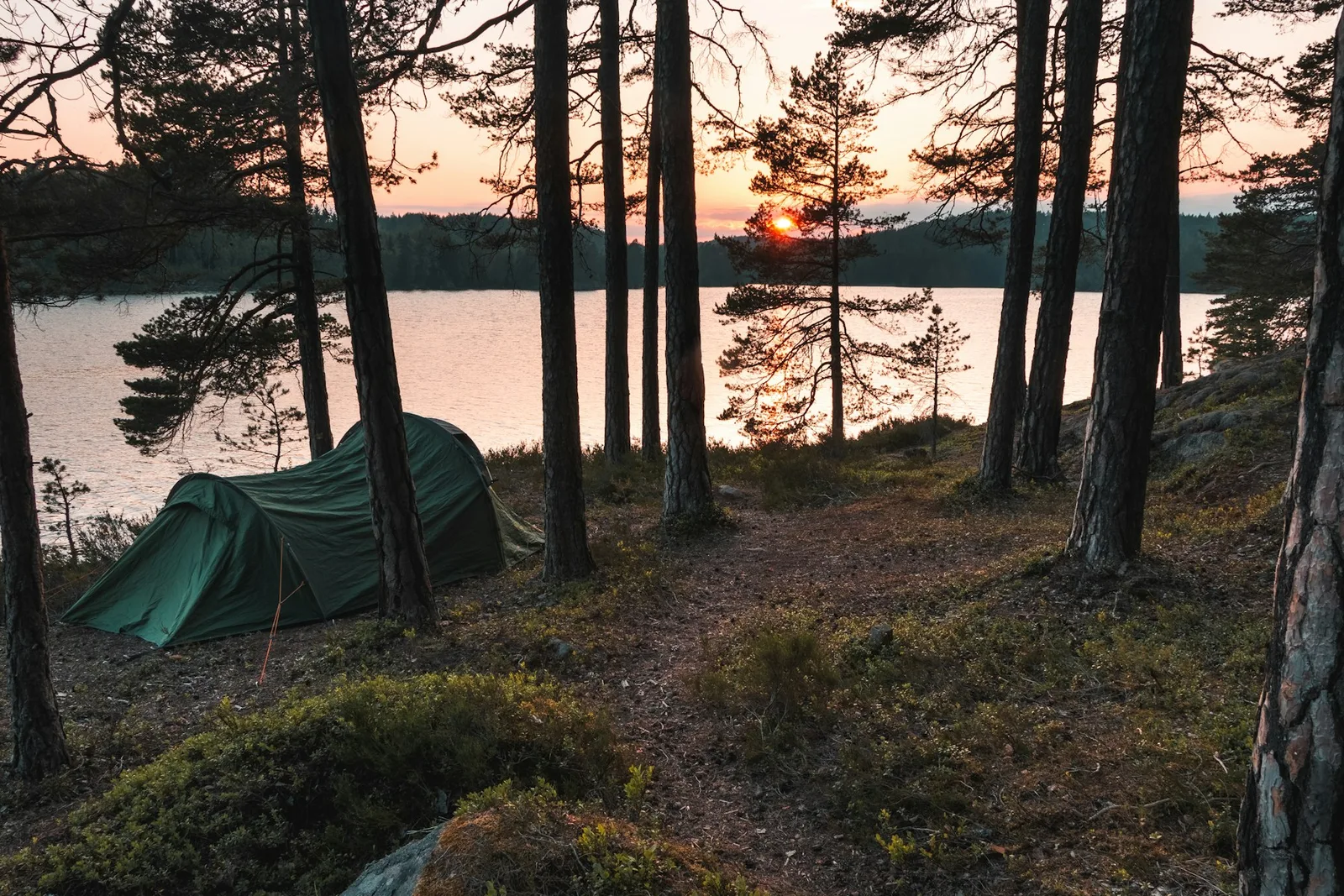 Grönt tält vid en sjö i solnedgång, nära Norrköping – illustrationsbild.