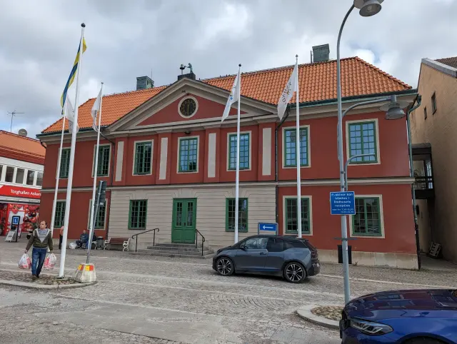 Rådhusets röda fasad med ljusa detaljer och flaggstänger vid torget i Askersund