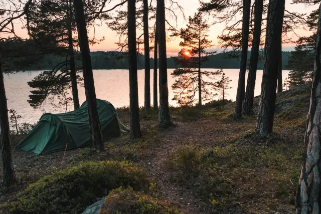 Grönt tält vid en sjö i solnedgång, nära Norrköping – illustrationsbild.